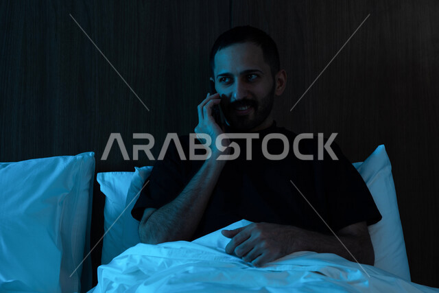 صوره مقربه لرجل عربي خليجي سعودي مستلقي على فراشه،  إستخدام الهاتف المحمول قبل النوم, تصفح الإنترنت, التواصل الإجتماعي, إنجاز المهام قبل النوم، استخدام تقنيات حديثة