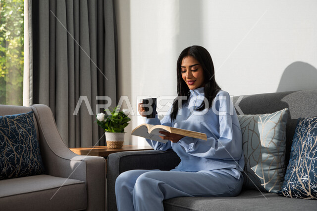 مرأة عربية خليجية سعودية تجلس في المنزل ، إحتساء القهوة ، قراءة القصص والروايات ، قضاء أوقات الفراغ في المنزل ، جلسات هادئة في المنزل ، الإستمتاع بقراءة  الكتب ، أنشطة ترفيهية