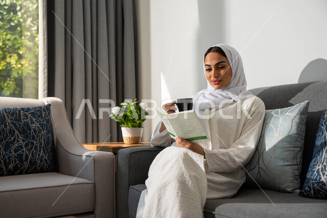 مرأة عربية خليجية سعودية تجلس في المنزل ، إحتساء القهوة ، قراءة القصص والروايات ، قضاء أوقات الفراغ في المنزل ، جلسات هادئة في المنزل ، الإستمتاع بقراءة  الكتب ، أنشطة ترفيهية