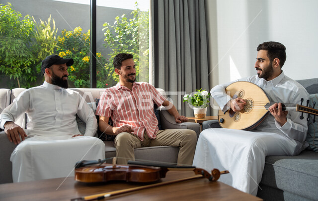 مجموعة من الأصدقاء العرب السعوديين يجلسون في المنزل، العزف آلة العود، توثيق اللحظات عبر الجوال، قضاء أوقات ممتعة مع الأصدقاء، جلسة وناسة وطرب، مواهب فنية، الفنون الموسيقية، آلات موسيقية، أنشطة ترفيهية، زيارات الأهل والأقارب