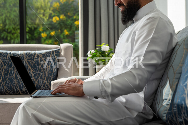 رجل عربي خليجي سعودي يجلس في المنزل، إستخدام جهاز الحاسوب المحمول، تصفح الإنترنت، جلسة عمل، العمل عن بعد، عقد إجتماع عمل عبر الإنترنت، التسويق الإلكتروني، مهن ووظائف، إجراء مكالمة فيديو، مشاهدة الأفلام والمسلسلات، بث مباشر