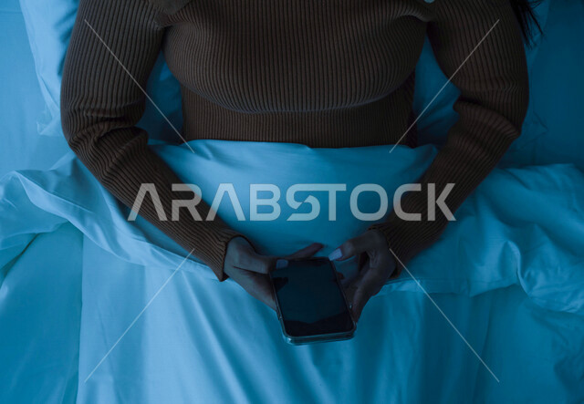 A close-up of a Saudi Arabian Gulf woman wearing warm winter clothes and using a mobile phone, surfing the Internet, social communication, the concept of comfort and tranquility, enjoying leisure time, using modern technologies