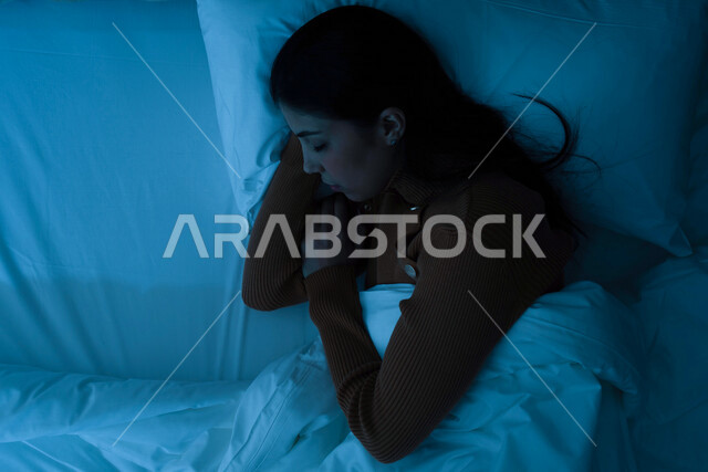 امرأة عربية خليجية سعودية ترتدي ملابس الشتاء الدافئة اثناء النوم، وقت النوم، النوم المبكر، وسادة بيضاء ناعمة، الاسترخاء والراحة، الاستمتاع بنوم هادئ وصحي