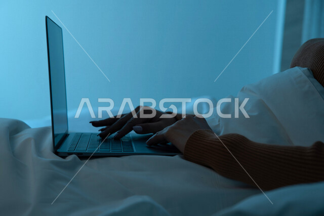 صورة مقربة لامرأة عربية خليجية سعودية ترتدي ملابس الشتاء الدافئة وتستخدم الحاسوب المحمول، تصفح الانترنت، التواصل الاجتماعي والدردشة، مفهوم الراحة والهدوء، الإستمتاع بقضاء أوقات الفراغ، استخدام تقنيات حديثة