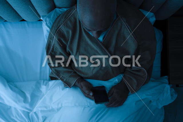 An elderly Saudi Arabian Gulf man wearing warm winter clothes, using a mobile phone, surfing the Internet, social communication, wearing a winter coat, the concept of comfort and tranquility, enjoying leisure time, using modern technologies