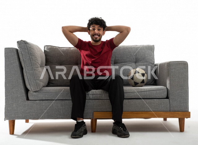 بورتريه لشاب عربي خليجي يرتدي تيشرت عنابي وبجانبه كرة القدم، الاستمتاع بمتابعة مباراة كرة قدم، إيماءات وجه ويدين تدل على الدهشة والذهول، الخسارة والخذلان، كأس العالم 2022، مونديال قطر، خلفية بيضاء