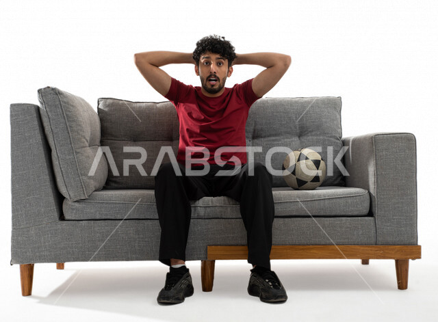 بورتريه لشاب عربي خليجي يرتدي تيشرت عنابي وبجانبه كرة القدم، الاستمتاع بمتابعة مباراة كرة قدم، إيماءات وجه ويدين تدل على الدهشة والذهول، الخسارة والخذلان، كأس العالم 2022، مونديال قطر، خلفية بيضاء