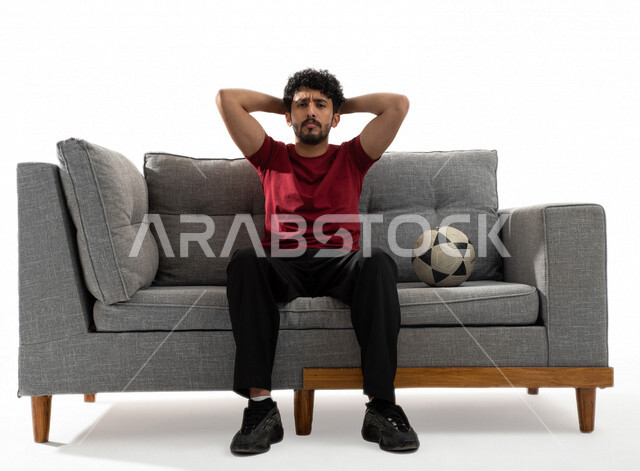 بورتريه لشاب عربي خليجي يرتدي تيشرت عنابي وبجانبه كرة القدم، الاستمتاع بمتابعة مباراة كرة قدم، إيماءات وجه ويدين تدل على الدهشة والذهول، الخسارة والخذلان، كأس العالم 2022، مونديال قطر، خلفية بيضاء