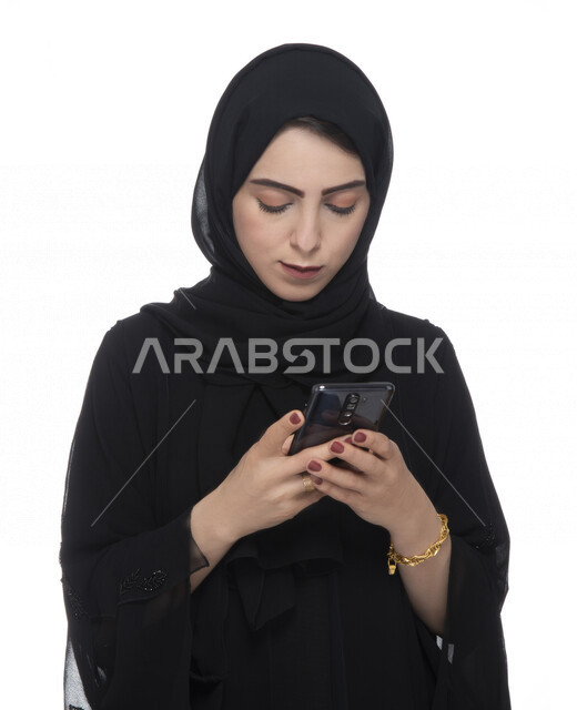 بورتريه لسيدة أعمال عربية خليجية إماراتية  ، تستخدام الهاتف المحمول بإيماءات وجه تدل على التركيز , العمل عن بعد، مفهوم إستخدام التكنلوجيا وأجهزة التقنية الحديثة، التسلية والترفيه، حجز طلبات الأونلاين ، التسويق الإلكتروني، عقد صفقات عبر الجوال , خلفيةبيضاء