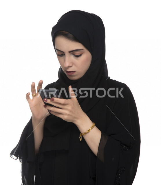 Portrait of an Arab Gulf Emirati businesswoman, using a mobile phone, working remotely, the concept of using technology and modern technical devices, entertainment and entertainment, booking online orders, e-marketing, making deals via mobile phone, white