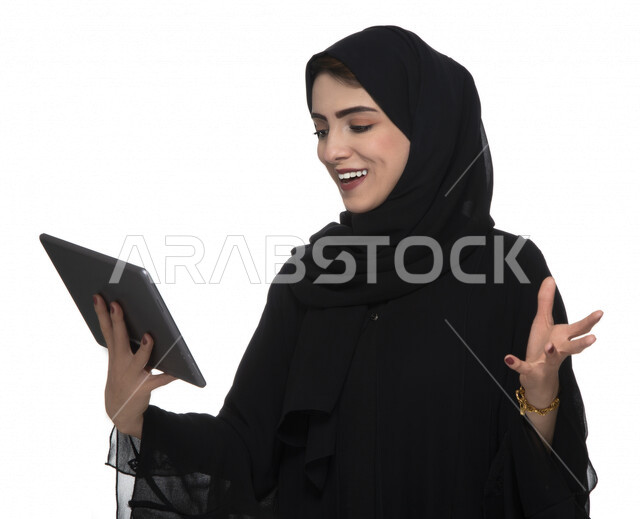 بورتريه لإمرأة عربيه خليجيه إماراتية بالزي التقليدي تستخدم جهاز لوحي بإيماءات وجه تدل على الفرح ,  ، التسويق الإلكتروني ، مفهوم التكنولوجيا وإستخدام الأجهزة التقنية الحديثة ، العمل عن بعد  , مكالمة فيديو , مشاهدة البرامج , خلفية بيضاء 
