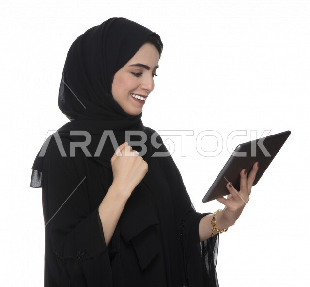 بورتريه لإمرأة عربيه خليجيه إماراتية بالزي التقليدي تستخدم جهاز لوحي بإيماءات وجه تدل على الفرح ,  ، التسويق الإلكتروني ، مفهوم التكنولوجيا وإستخدام الأجهزة التقنية الحديثة ، العمل عن بعد  , مكالمة فيديو , مشاهدة البرامج , خلفية بيضاء 