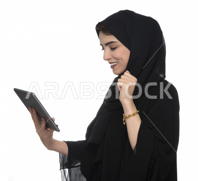 بورتريه لإمرأة عربيه خليجيه إماراتية بالزي التقليدي تستخدم جهاز لوحي بإيماءات وجه تدل على الفرح ,  ، التسويق الإلكتروني ، مفهوم التكنولوجيا وإستخدام الأجهزة التقنية الحديثة ، العمل عن بعد  , مكالمة فيديو , مشاهدة البرامج , خلفية بيضاء 