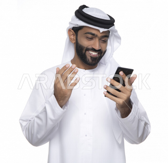 بورتريه لشاب عربي خليجي إماراتي يستعمل هاتف المحمول ، إيماءات وجه تدل على الفرح والسعادة , التواصل مع الأفراد ، طلبات أونلاين و تسويق ، علاقات اجتماعية  ، استخدام أجهزة تقنية ، خلفية بيضاء