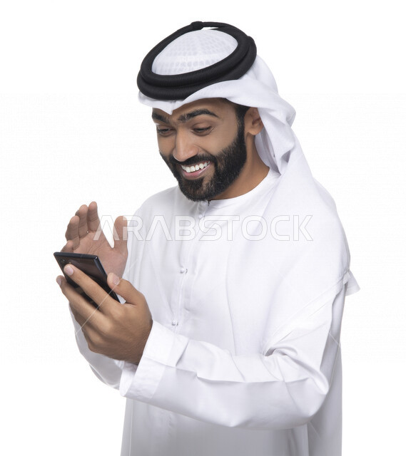 Portrait of an Arab Gulf Emirati youth using a mobile phone, facial gestures indicating joy and happiness, communication with individuals, online orders and marketing, social relations, use of technical devices, white background