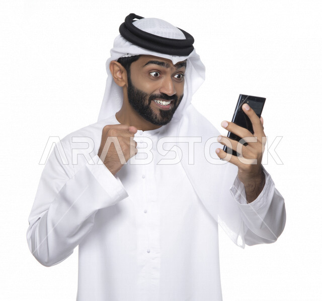 بورتريه لشاب عربي خليجي إماراتي يستعمل هاتف المحمول ، إيماءات وجه تدل على الفرح والسعادة , التواصل مع الأفراد ، طلبات أونلاين و تسويق ، علاقات اجتماعية  ، استخدام أجهزة تقنية ، خلفية بيضاء
