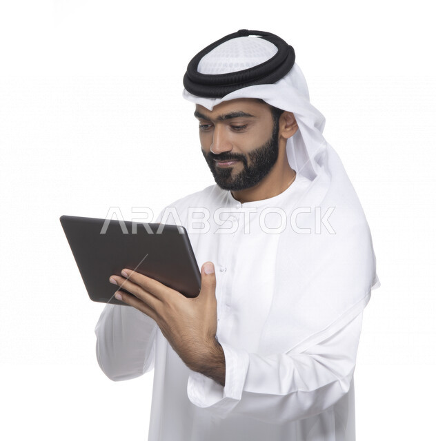 Portrait of an Arab Gulf Emirati man in traditional dress using a tablet, e-marketing, the concept of technology and the use of modern technical devices, remote work, video call, watching programs, white background