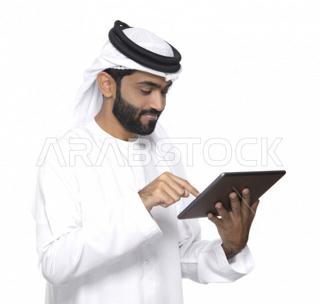بورتريه لرجل عربي خليجي إماراتي بالزي التقليدي  يستخدم جهاز لوحي  ، التسويق الإلكتروني ، مفهوم التكنولوجيا وإستخدام الأجهزة التقنية الحديثة ، العمل عن بعد  , مكالمة فيديو , مشاهدة البرامج , خلفية بيضاء 