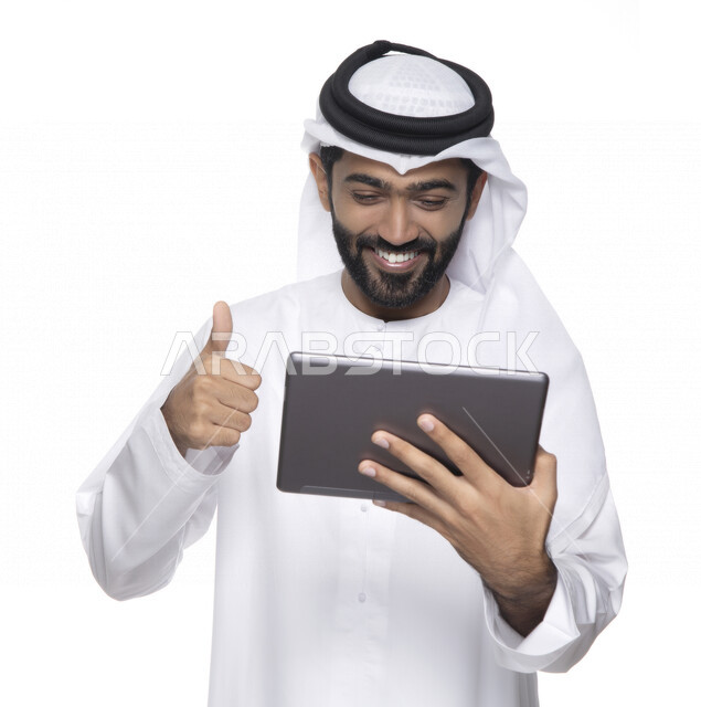 بورتريه لرجل عربي خليجي إماراتي بالزي التقليدي  يستخدم جهاز لوحي ويأشر بأصبع الإبهام للأعلى , ايماءات تدل على الإعجاب  ، التسويق الإلكتروني ، العمل عن بعد  , مكالمة فيديو , مشاهدة البرامج , خلفية بيضاء 