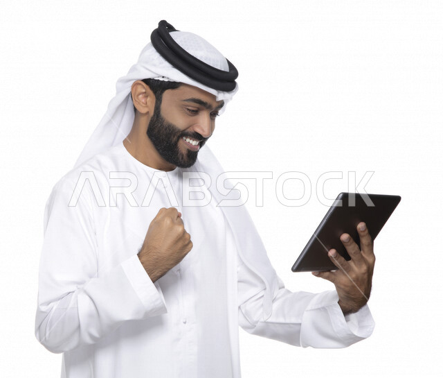 Portrait of an Arab Gulf Emirati man in traditional dress using a tablet, e-marketing, the concept of technology and the use of modern technical devices, remote work, video call, watching programs, white background