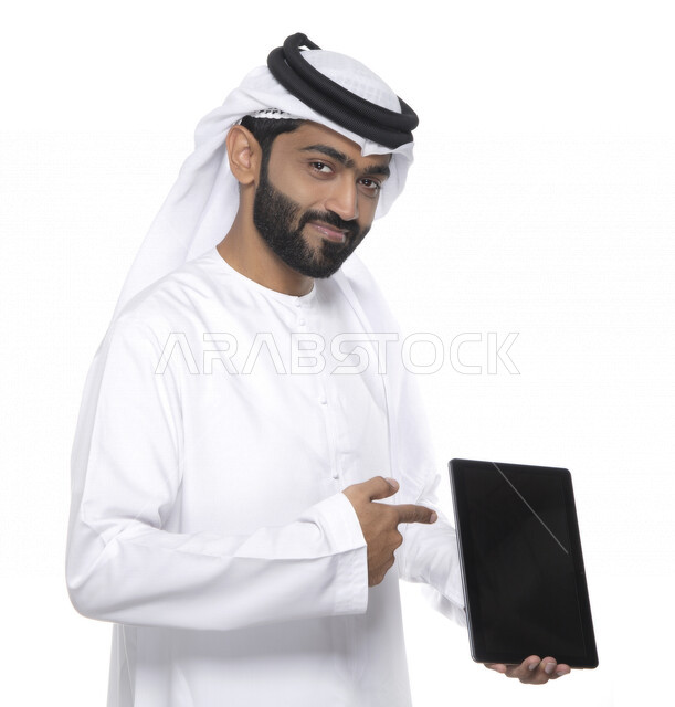Portrait of an Arab Gulf Emirati man in traditional dress using a tablet, e-marketing, the concept of technology and the use of modern technical devices, remote work, video call, watching programs, white background
