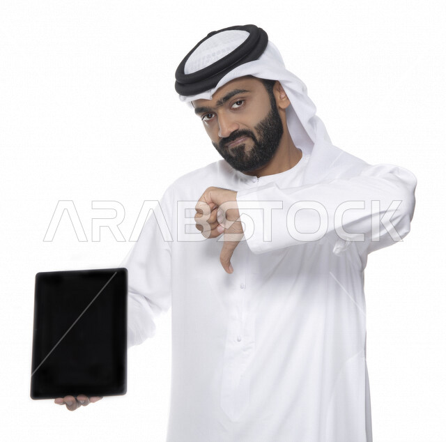 بورتريه لرجل عربي خليجي إماراتي بالزي التقليدي  يستخدم جهاز لوحي ويأشر بأصبع الإبهام للأسفل  ، إيماءات تدل على عدم الإعجاب  ، مفهوم التكنولوجيا وإستخدام الأجهزة التقنية الحديثة ، العمل عن بعد  , مشاهدة البرامج , خلفية بيضاء 