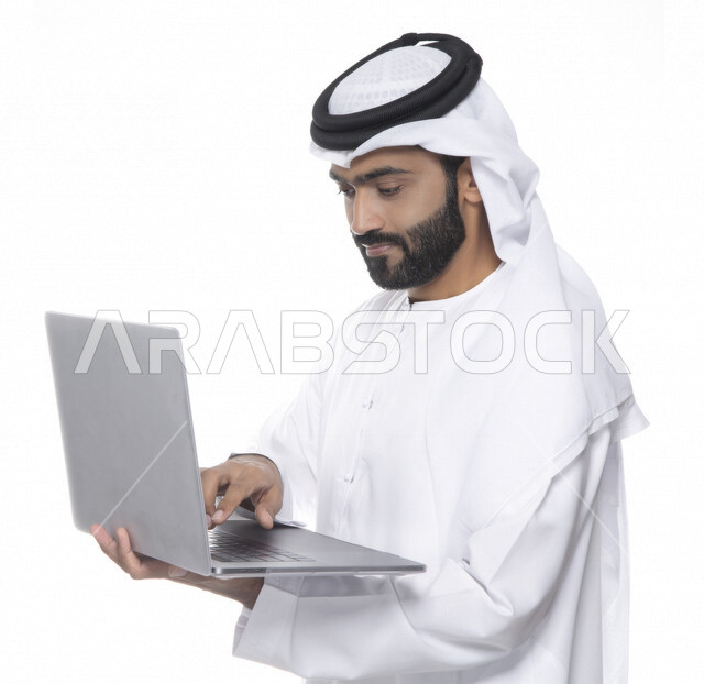 بورتريه لرجل أعمال عربي خليجي إماراتي يستخدم جهاز الحاسوب المحمول لإنجاز المهام، جلسة عمل، إنجاز المشاريع والمهام، مهن وأعمال تجارية، متابعة ومناقشة العمل، عقد إجتماع عمل عبر الإنترنت، التسويق الإلكتروني، خلفية بيضاء 