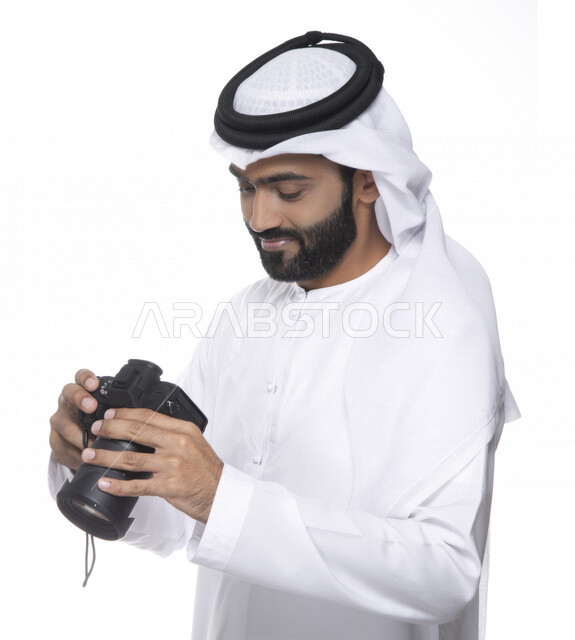 بورتريه لشاب عربي خليجي إماراتي ، يحمل بيده كاميرا التصوير ، يلتقط الصور باستخدام كاميرا التصوير ، التصوير الفوتوغرافي ، موهبة واحتراف فن التصوير ، مصور إماراتي  ، كاميرا عالية الدقة ، خلفية بيضاء 