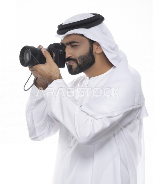 بورتريه لشاب عربي خليجي إماراتي ، يحمل بيده كاميرا التصوير ، يلتقط الصور باستخدام كاميرا التصوير ، التصوير الفوتوغرافي ، موهبة واحتراف فن التصوير ، مصور إماراتي  ، كاميرا عالية الدقة ، خلفية بيضاء 