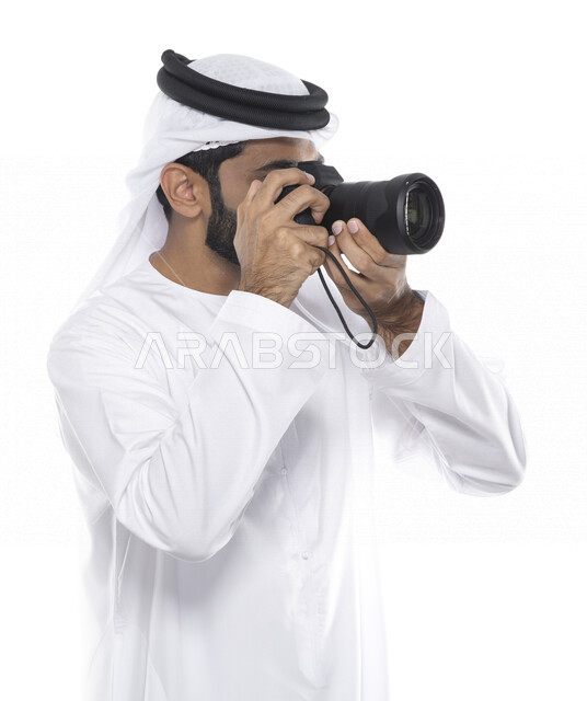 بورتريه لشاب عربي خليجي إماراتي ، يحمل بيده كاميرا التصوير ، يلتقط الصور باستخدام كاميرا التصوير ، التصوير الفوتوغرافي ، موهبة واحتراف فن التصوير ، مصور إماراتي  ، كاميرا عالية الدقة ، خلفية بيضاء 