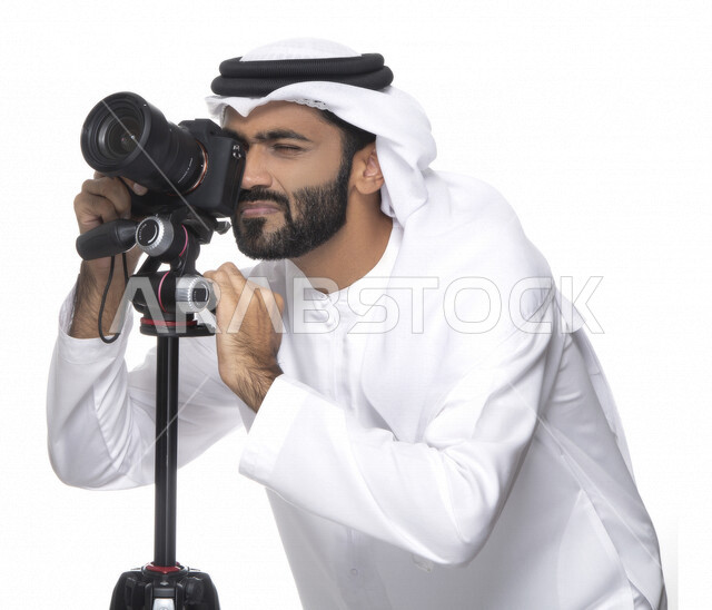 بورتريه لشاب عربي خليجي إماراتي ، يحمل بيده كاميرا التصوير ، يلتقط الصور باستخدام كاميرا التصوير ، التصوير الفوتوغرافي ، موهبة واحتراف فن التصوير ، مصور إماراتي  ، كاميرا عالية الدقة ، خلفية بيضاء 