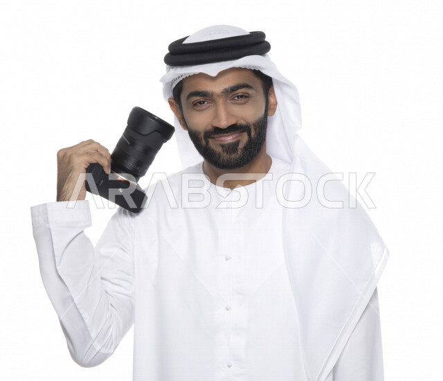 بورتريه لشاب عربي خليجي إماراتي ، يحمل بيده كاميرا التصوير ، يلتقط الصور باستخدام كاميرا التصوير ، التصوير الفوتوغرافي ، موهبة واحتراف فن التصوير ، مصور إماراتي  ، كاميرا عالية الدقة ، خلفية بيضاء 