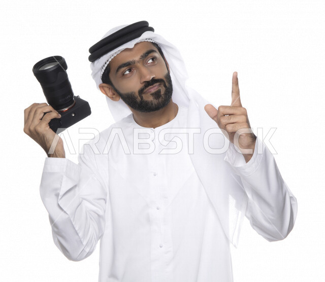بورتريه لشاب عربي خليجي إماراتي ، يحمل بيده كاميرا التصوير ، يلتقط الصور باستخدام كاميرا التصوير ، التصوير الفوتوغرافي ، موهبة واحتراف فن التصوير ، مصور إماراتي  ، كاميرا عالية الدقة ، خلفية بيضاء 