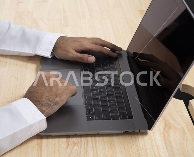 صورة مقربة لرجل عربي خليجي إماراتي  يستخدم جهاز الحاسوب المحمول لإنجاز المهام، جلسة عمل، إنجاز المشاريع والمهام، مهن وأعمال تجارية، متابعة ومناقشة العمل، عقد إجتماع عمل عبر الإنترنت 