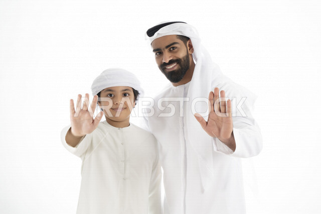 بورتريه لرجل عربي إماراتي خليجي يرتدي الزي التقليدي بجانب طفله , يأشران بيدهم عبارة لا للعنف الأسري  , إشارة يد توقف  ، تعابير وجه مبتسمة  ، خلفية بيضاء
