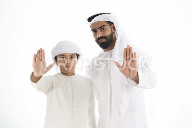 بورتريه لرجل عربي إماراتي خليجي يرتدي الزي التقليدي بجانب طفله , يأشران بيدهم عبارة لا للعنف الأسري  , إشارة يد توقف  ، تعابير وجه غاضبه  ، خلفية بيضاء