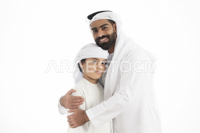 بورتريه لرجل عربي إماراتي خليجي يرتدي الزي التقليدي بجانب طفله , إماراتي يحضن ولده بكل حب وحنان    ، تجمع عائلي ، تعابير وجه مبتسمة  ، قضاء أوقات عائلية جميلة  ، خلفية بيضاء