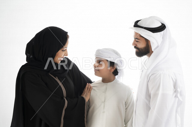 بورتريه لزوجان عربيان خليجيان إماراتيان بجانب إبنهم يرتديان  الزي الإماراتي التقليدي , قضاء وقت ممتع مع العائلة , إيماءات وجه تدل على السعادة والفرح , حضن الإبن , حنان وحب الأهل   , خلفية بيضاء 