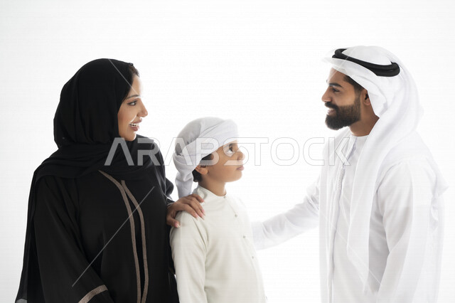 بورتريه لزوجان عربيان خليجيان إماراتيان بجانب إبنهم يرتديان  الزي الإماراتي التقليدي , قضاء وقت ممتع مع العائلة , إيماءات وجه تدل على السعادة والفرح , حضن الإبن , حنان وحب الأهل   , خلفية بيضاء 