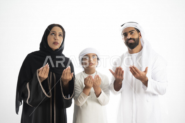 بورتريه لعائلة عربية إماراتية خليجية , ترتدي الزي التقليدي الإماراتي , يرفعان يدهم إلى الأعلى , الدعاء و التضرع لله , العبادة و تقرب الى الله تعالى في شهر رمضان المبارك , خلفية بيضاء 