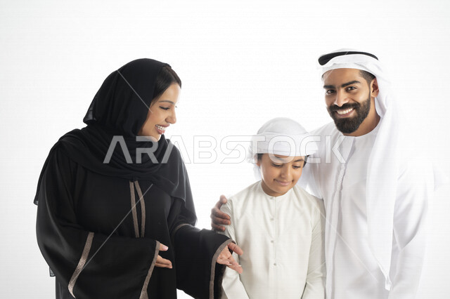 بورتريه لزوجان عربيان خليجيان إماراتيان بجانب إبنهم يرتديان  الزي الإماراتي التقليدي , قضاء وقت ممتع مع العائلة , إيماءات وجه تدل على السعادة والفرح , حضن الإبن , أم تمسك بخد ولدها بكل حب وحنان  , خلفية بيضاء 