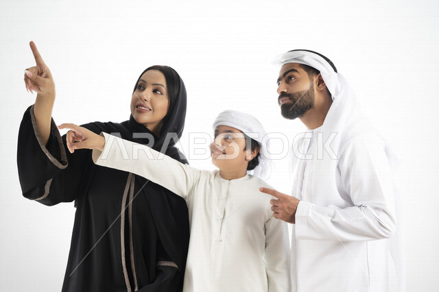 بورتريه لزوجان عربيان خليجيان إماراتيان بجانب إبنهم يرتديان  الزي الإماراتي التقليدي , قضاء وقت ممتع مع العائلة , إيماءات وجه تدل على السعادة والفرح ,يأشران بيدهم إلى الأعلى ,  خلفية بيضاء 