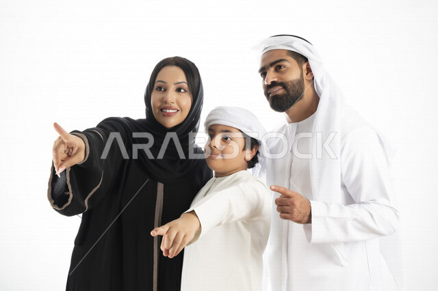 بورتريه لزوجان عربيان خليجيان إماراتيان بجانب إبنهم يرتديان  الزي الإماراتي التقليدي , قضاء وقت ممتع مع العائلة , إيماءات وجه تدل على السعادة والفرح ,يأشران بيدهم إلى الأعلى ,  خلفية بيضاء 