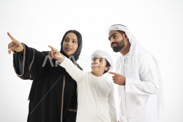 بورتريه لزوجان عربيان خليجيان إماراتيان بجانب إبنهم يرتديان  الزي الإماراتي التقليدي , قضاء وقت ممتع مع العائلة , إيماءات وجه تدل على السعادة والفرح ,يأشران بيدهم إلى الأعلى ,  خلفية بيضاء 