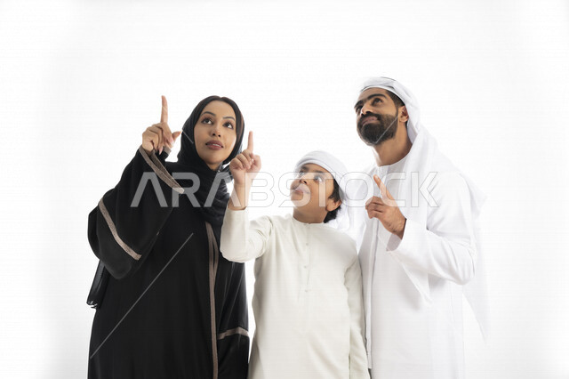 بورتريه لزوجان عربيان خليجيان إماراتيان بجانب إبنهم يرتديان  الزي الإماراتي التقليدي , قضاء وقت ممتع مع العائلة , إيماءات وجه تدل على السعادة والفرح ,يأشران بيدهم إلى الأعلى ,  خلفية بيضاء 