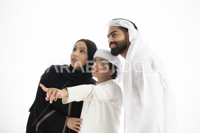 بورتريه لزوجان عربيان خليجيان إماراتيان بجانب إبنهم يرتديان  الزي الإماراتي التقليدي , قضاء وقت ممتع مع العائلة , إيماءات وجه تدل على السعادة والفرح ,يأشران بيدهم إلى الأعلى ,  خلفية بيضاء 