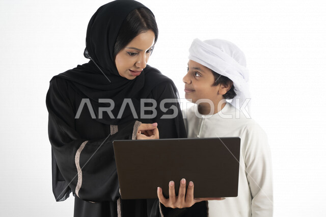 بورتريه لأم عربية خليجية إماراتية ترتدي الزي التقليدي الإماراتي شيلة وعباية ، تعليم الطفل كيفية استخدام الكمبيوتر في المدرسة، استخدام لوحة المفاتيح للكتابة، التعليم الالكتروني، التعليم الفعال، خلفية بيضاء 