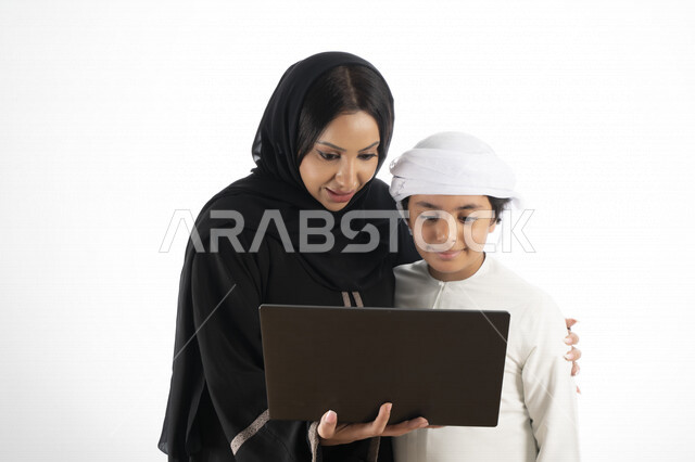 بورتريه لأم عربية خليجية إماراتية ترتدي الزي التقليدي الإماراتي شيلة وعباية ، تعليم الطفل كيفية استخدام الكمبيوتر في المدرسة، استخدام لوحة المفاتيح للكتابة، التعليم الالكتروني، التعليم الفعال، خلفية بيضاء 