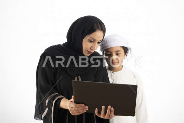 بورتريه لأم عربية خليجية إماراتية ترتدي الزي التقليدي الإماراتي شيلة وعباية ، تعليم الطفل كيفية استخدام الكمبيوتر في المدرسة، استخدام لوحة المفاتيح للكتابة، التعليم الالكتروني، التعليم الفعال، خلفية بيضاء 