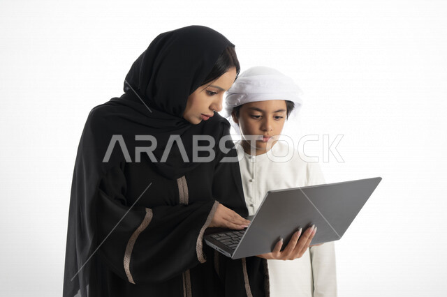 بورتريه لأم عربية خليجية إماراتية ترتدي الزي التقليدي الإماراتي شيلة وعباية ، تعليم الطفل كيفية استخدام الكمبيوتر في المدرسة، استخدام لوحة المفاتيح للكتابة، التعليم الالكتروني، التعليم الفعال، خلفية بيضاء 